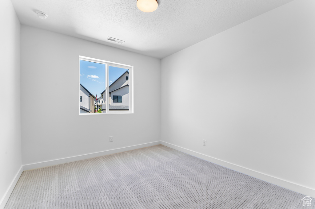 Spare room with light colored carpet, baseboards, and a textured ceiling