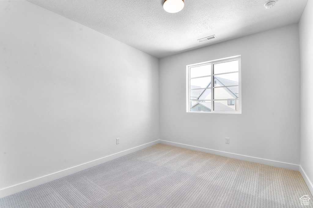 Empty room with light carpet, a textured ceiling, and baseboards