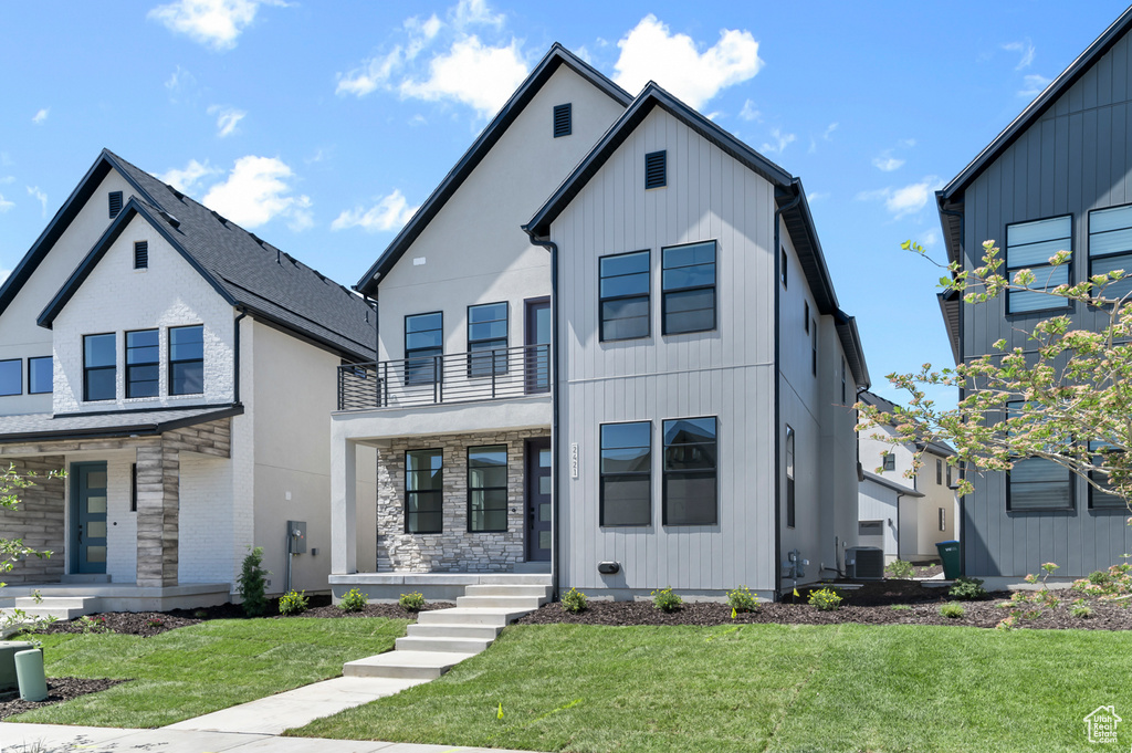 View of front of home featuring stone siding, a balcony, covered porch, and a front lawn