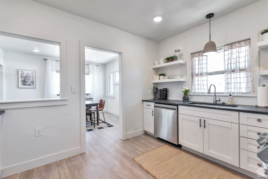 Kitchen with sink, white cabinetry, hanging light fixtures, light wood-type flooring, and stainless steel dishwasher