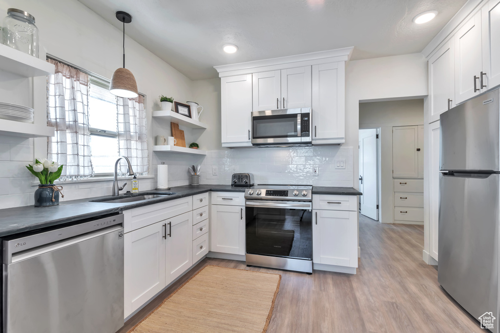 Kitchen with stainless steel appliances, white cabinetry, hanging light fixtures, and sink