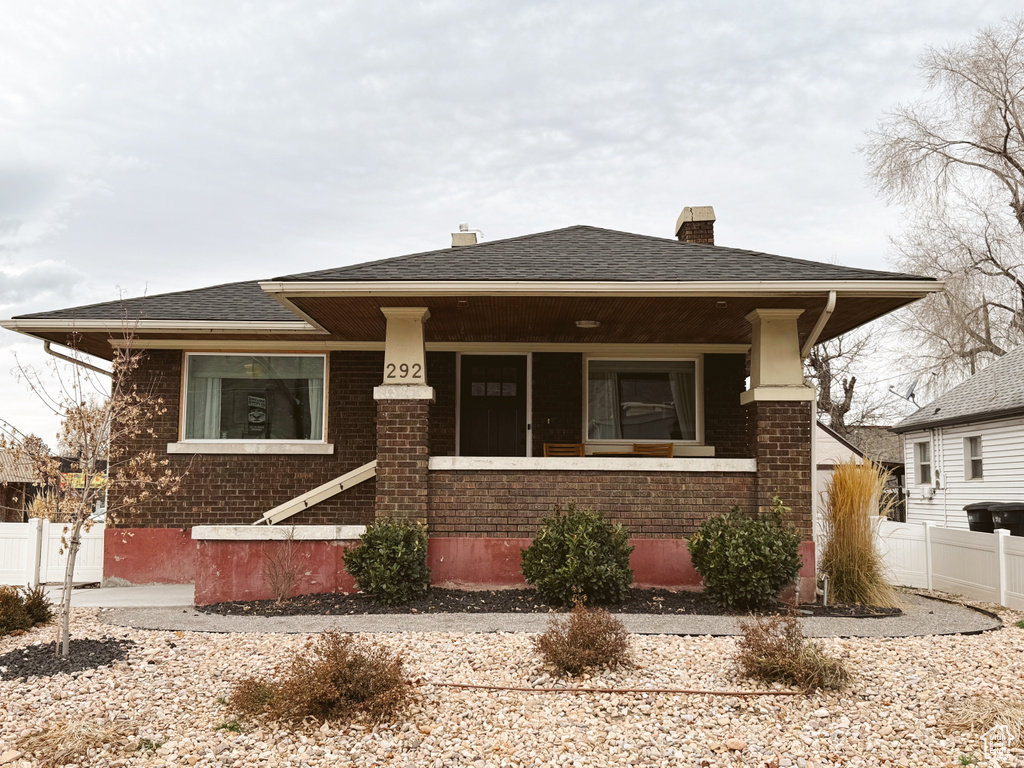 View of front facade featuring brick siding, fence, a shingled roof, and a chimney