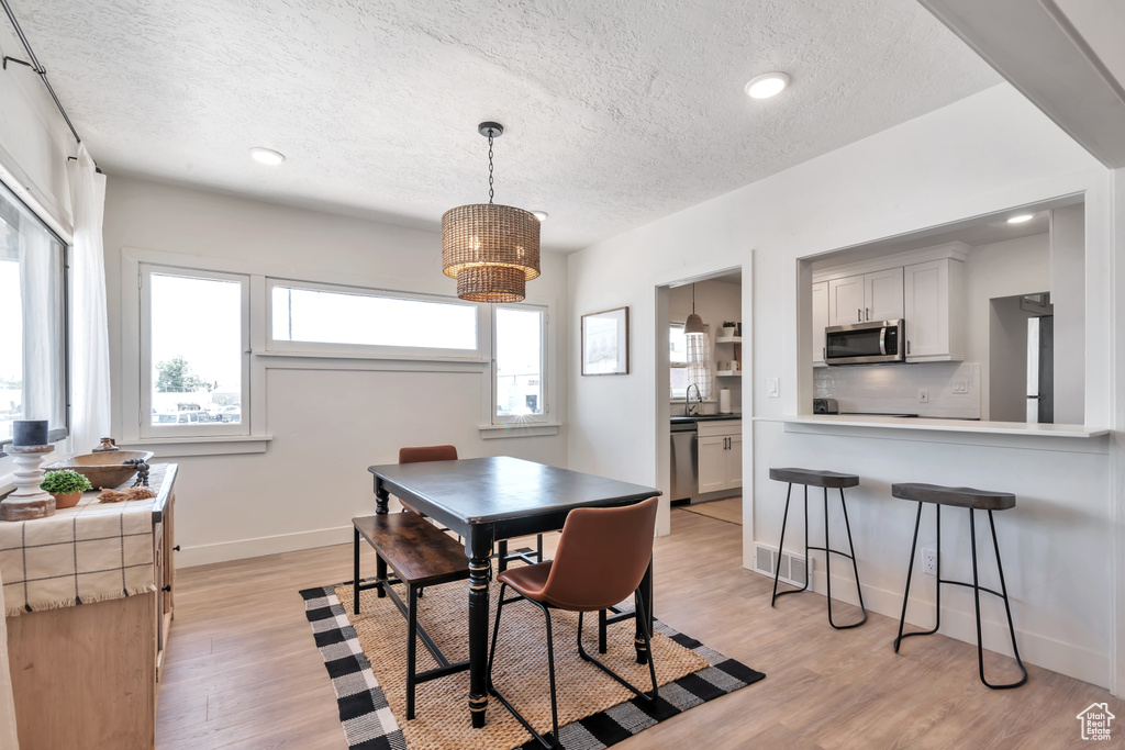 Dining room with a chandelier, sink, a textured ceiling, and light wood-type flooring