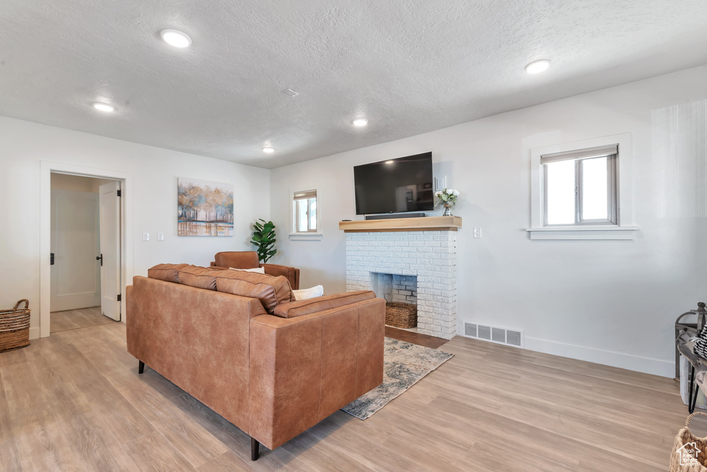 Living room with light hardwood / wood-style floors, a brick fireplace, and a textured ceiling