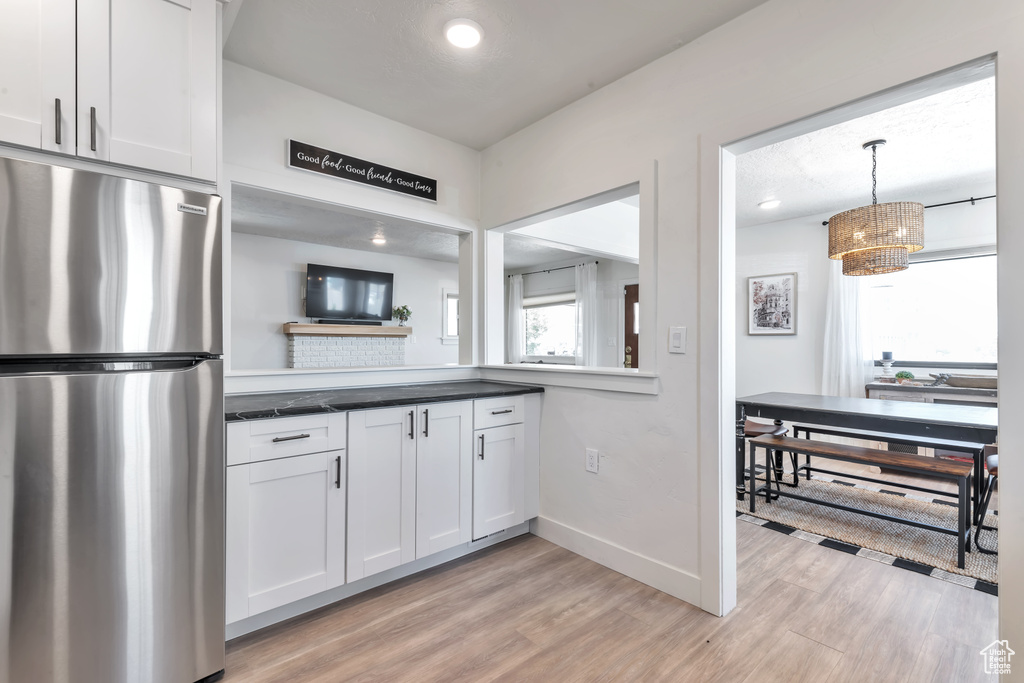 Kitchen featuring white cabinetry, stainless steel fridge, light wood-type flooring, and decorative light fixtures