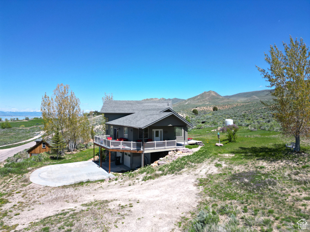 View of side of property with a deck with mountain view, driveway, and roof with shingles