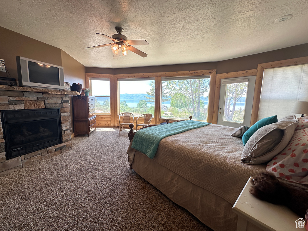 Bedroom featuring carpet floors, a textured ceiling, a stone fireplace, a ceiling fan, and access to outside