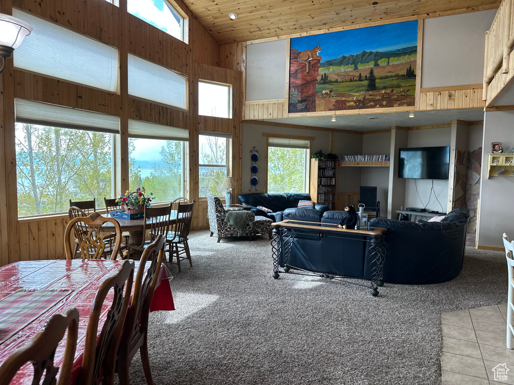 Living area with high vaulted ceiling, light colored carpet, wood walls, and light tile patterned flooring