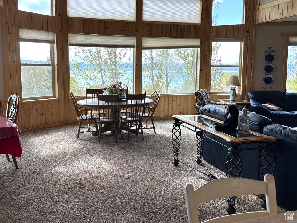 Carpeted dining area with healthy amount of natural light, wooden walls, and a towering ceiling