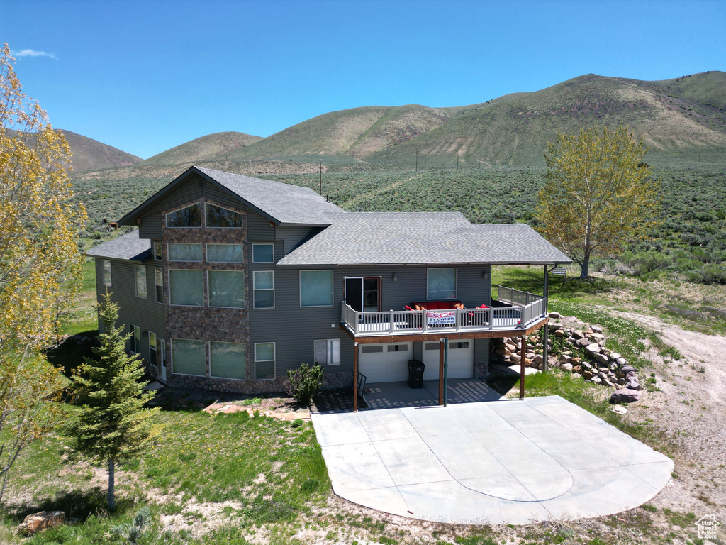 Rear view of property with an attached garage, driveway, a mountain view, stone siding, and a shingled roof