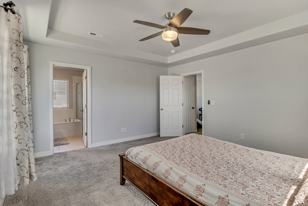 Carpeted bedroom featuring a tray ceiling, baseboards, connected bathroom, and ceiling fan