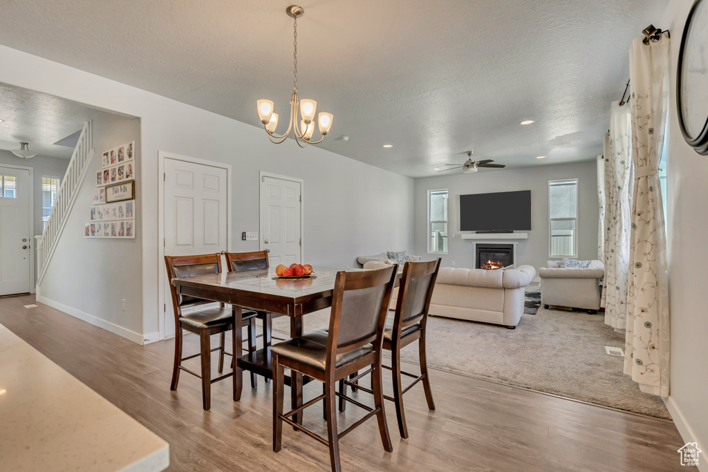 Dining area with light wood-type flooring, baseboards, a glass covered fireplace, a ceiling fan, and a textured ceiling