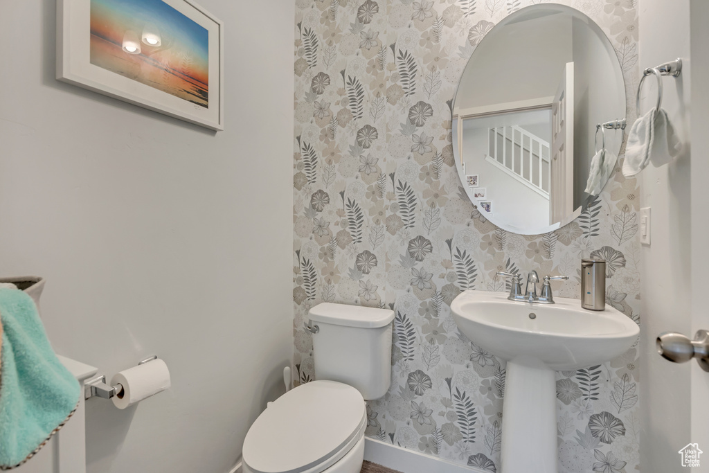 Half bathroom with toilet, wallpapered walls, a sink, and baseboards