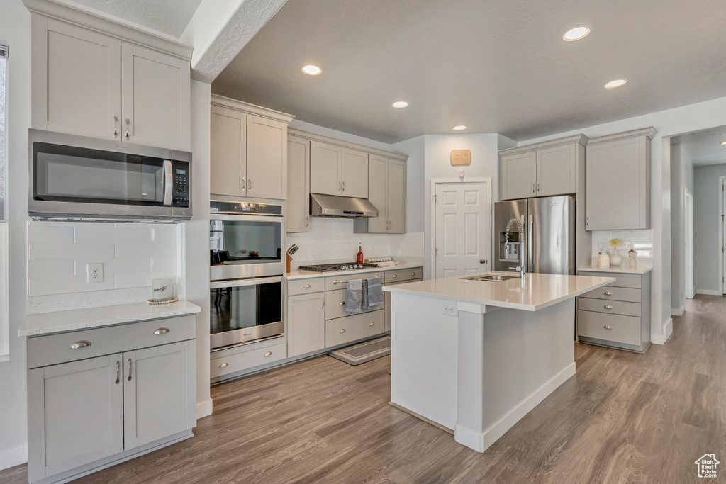 Kitchen featuring stainless steel appliances, light wood-style flooring, gray cabinetry, light countertops, and recessed lighting