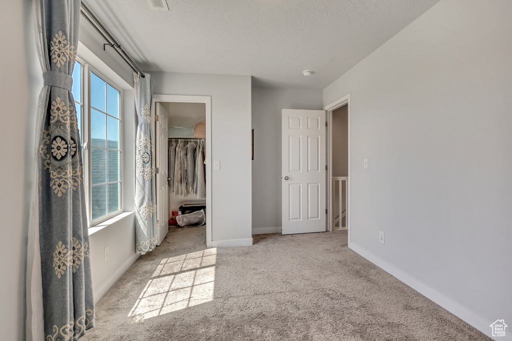 Unfurnished bedroom with multiple windows, carpet floors, baseboards, a textured ceiling, and a spacious closet