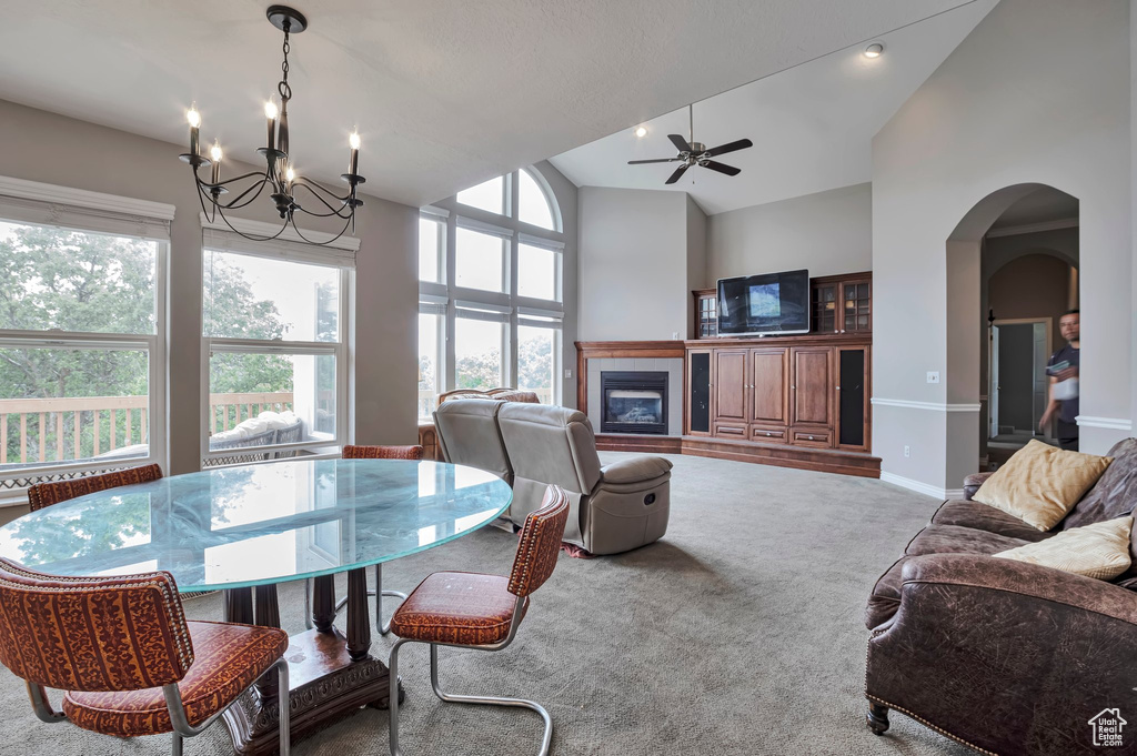 Dining area featuring a chandelier, carpet, a tiled fireplace, arched walkways, and ceiling fan