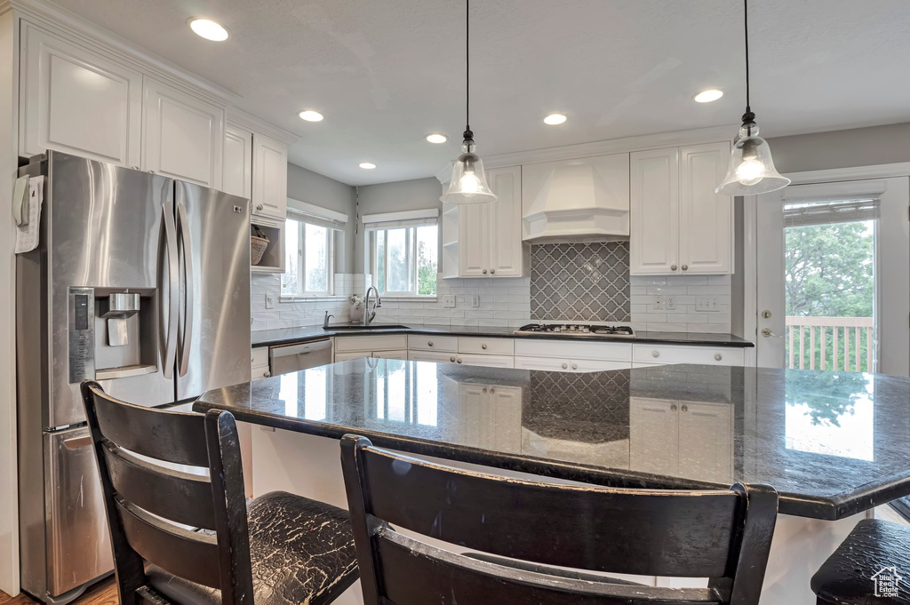 Kitchen featuring appliances with stainless steel finishes, custom range hood, a sink, white cabinets, and recessed lighting