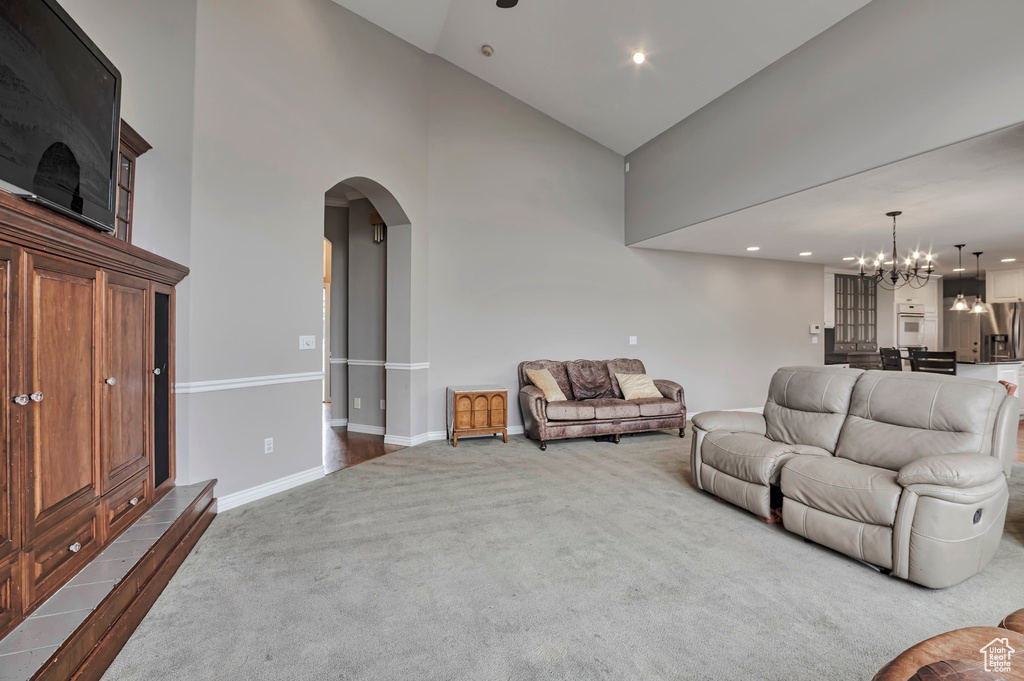 Living room with high vaulted ceiling, carpet flooring, a chandelier, arched walkways, and baseboards
