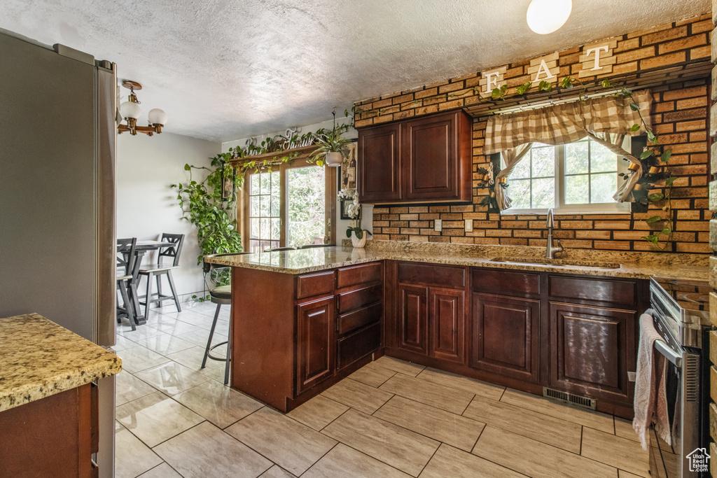 Kitchen featuring a sink, a textured ceiling, a peninsula, healthy amount of natural light, and light stone countertops