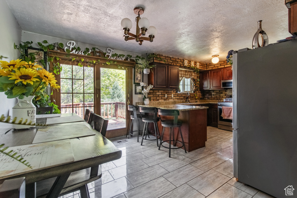 Kitchen featuring stainless steel appliances, a peninsula, plenty of natural light, a chandelier, and a textured ceiling