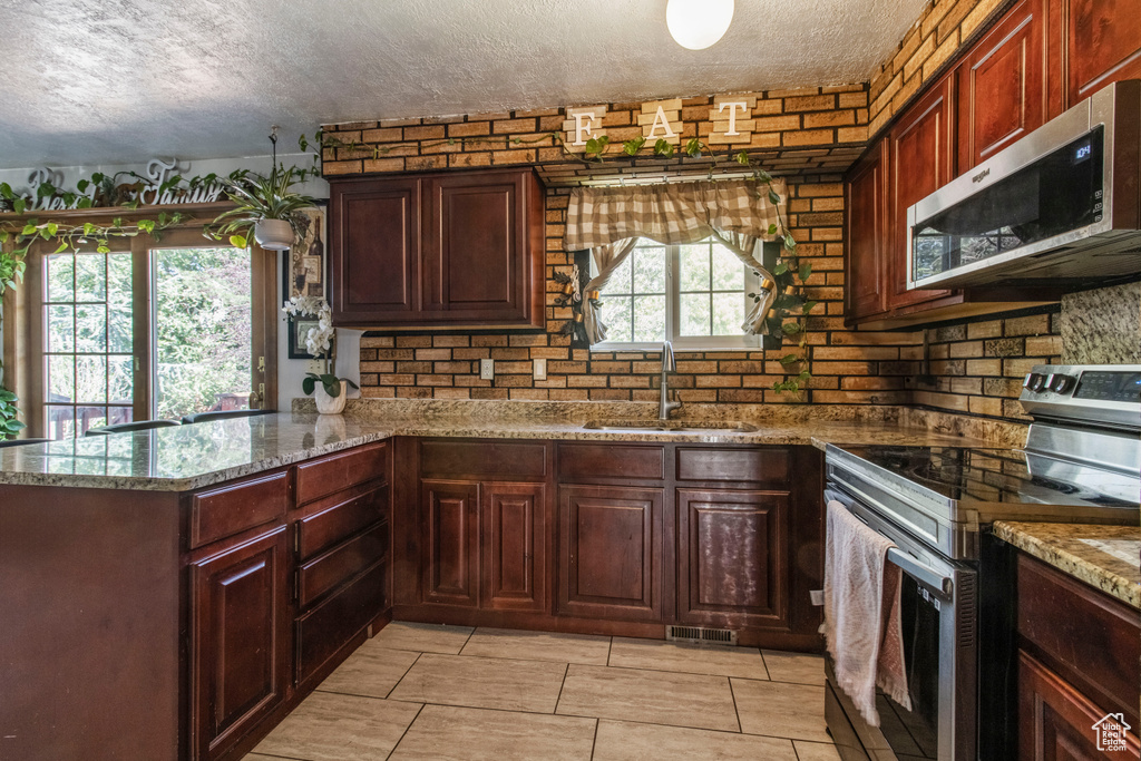 Kitchen with appliances with stainless steel finishes, a sink, a textured ceiling, a peninsula, and light stone countertops