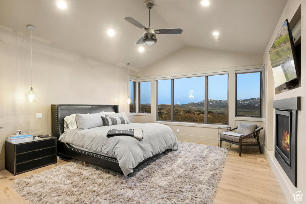 Bedroom featuring lofted ceiling, light wood-type flooring, a glass covered fireplace, and recessed lighting