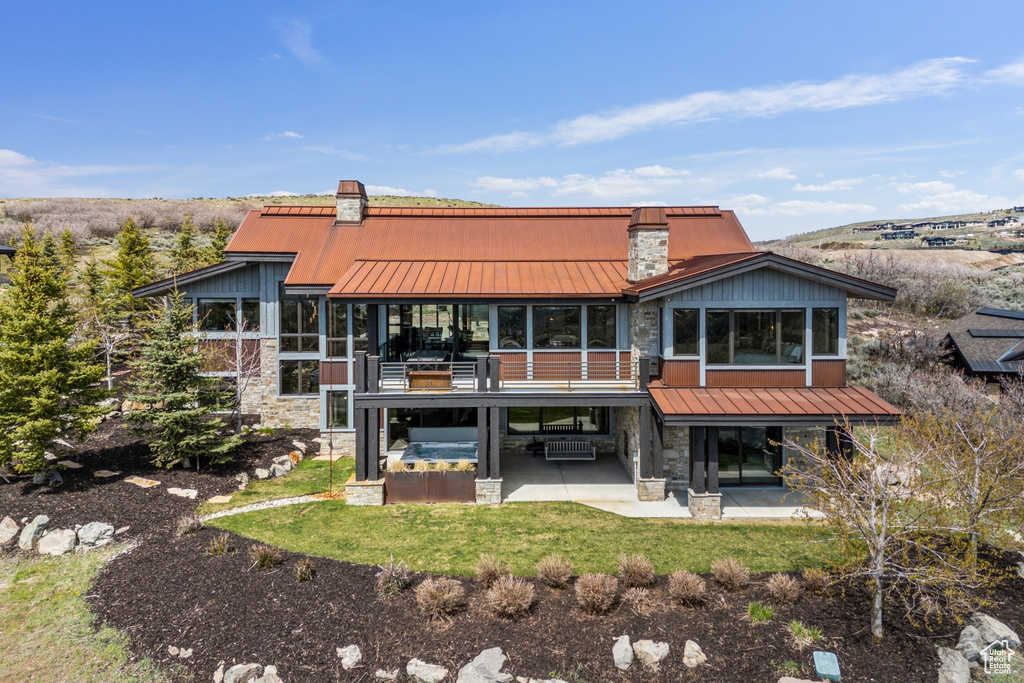 Back of property featuring stone siding, a patio area, and a standing seam roof