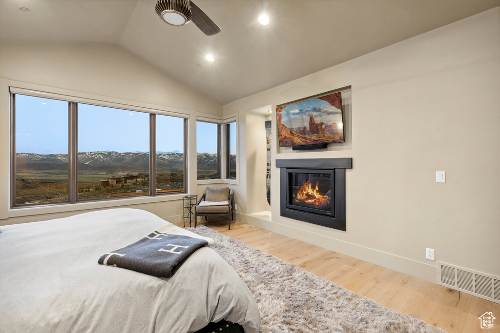 Bedroom with lofted ceiling, recessed lighting, a glass covered fireplace, visible vents, and wood finished floors