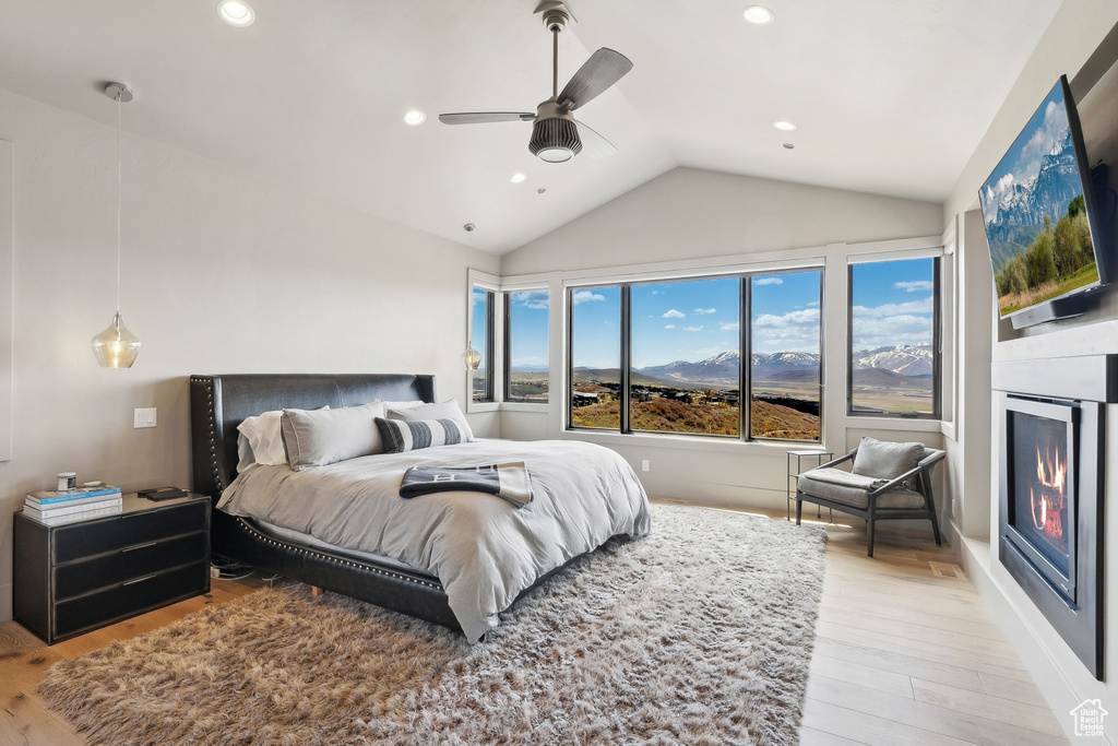 Bedroom with recessed lighting, light wood-style flooring, lofted ceiling, and a glass covered fireplace