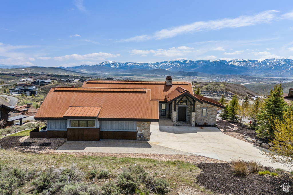 View of front of house with stone siding, a mountain view, a chimney, metal roof, and driveway