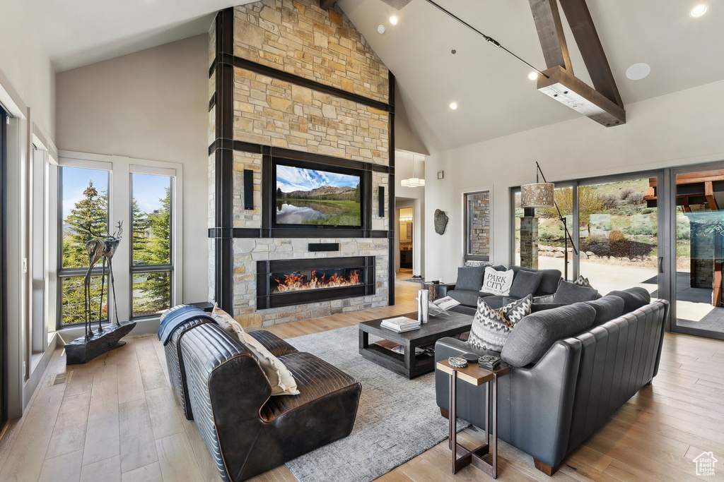 Living area featuring a stone fireplace, beam ceiling, high vaulted ceiling, and wood finished floors