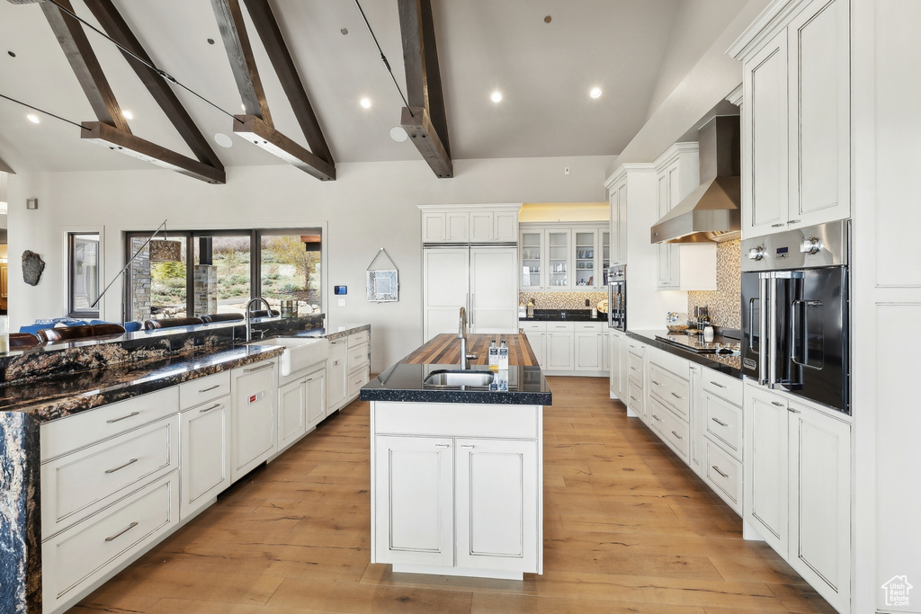 Kitchen with wall oven, wall chimney exhaust hood, beamed ceiling, and a sink
