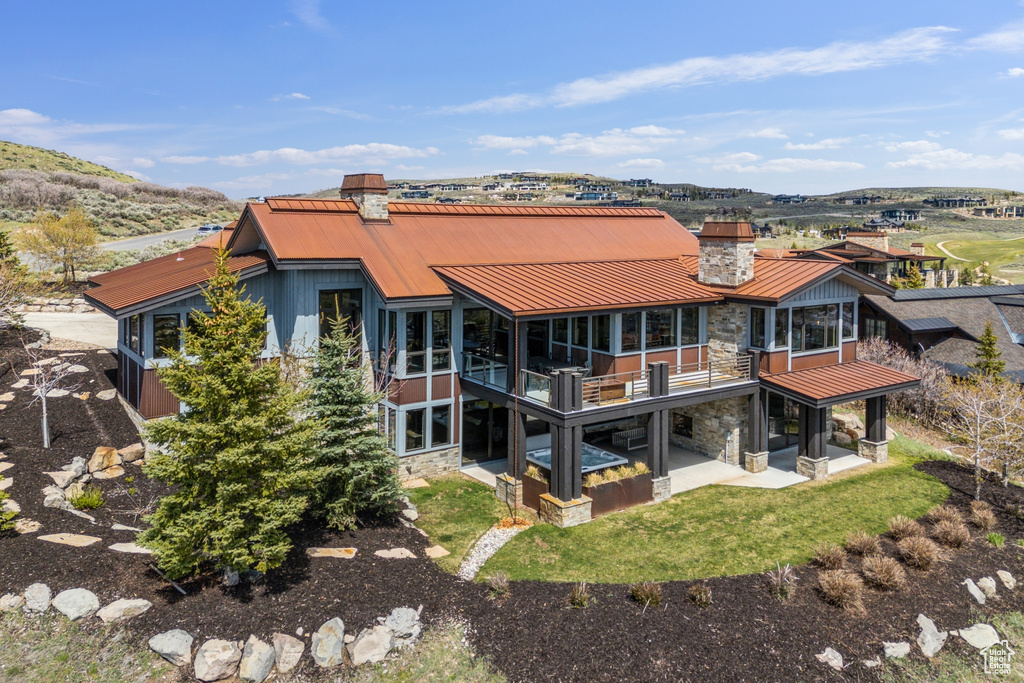Rear view of property featuring stone siding, a patio, metal roof, a chimney, and a standing seam roof