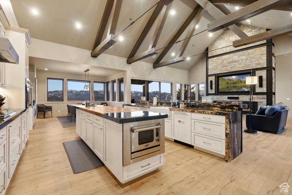 Kitchen featuring a sink, open floor plan, stainless steel microwave, beamed ceiling, and a spacious island