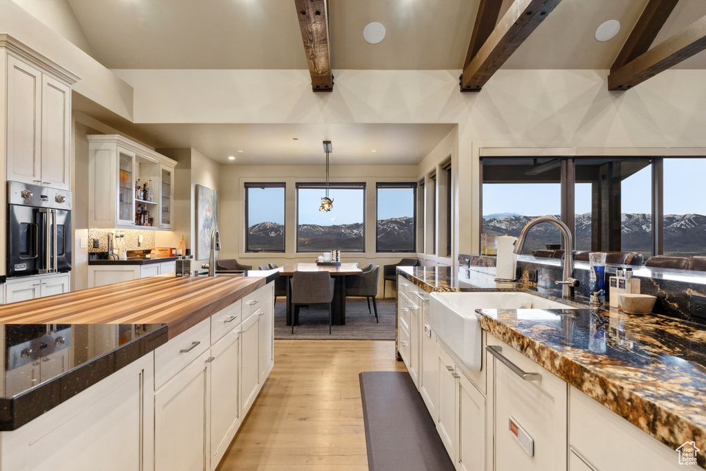 Kitchen featuring a sink, oven, light wood-type flooring, beamed ceiling, and butcher block counters