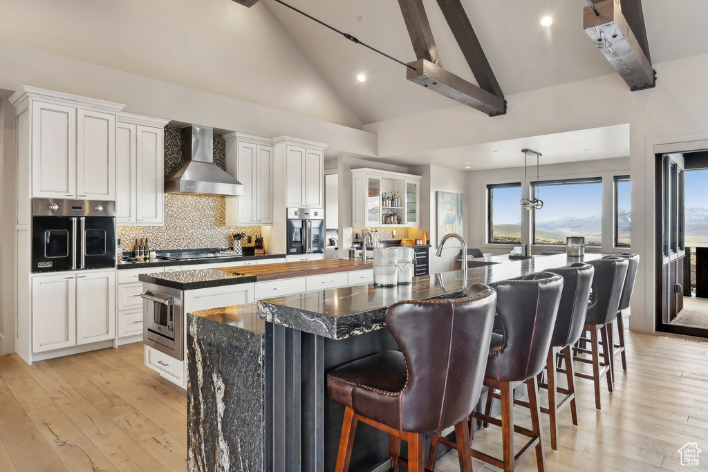 Kitchen with wall chimney exhaust hood, a spacious island, light wood-style flooring, and stainless steel oven
