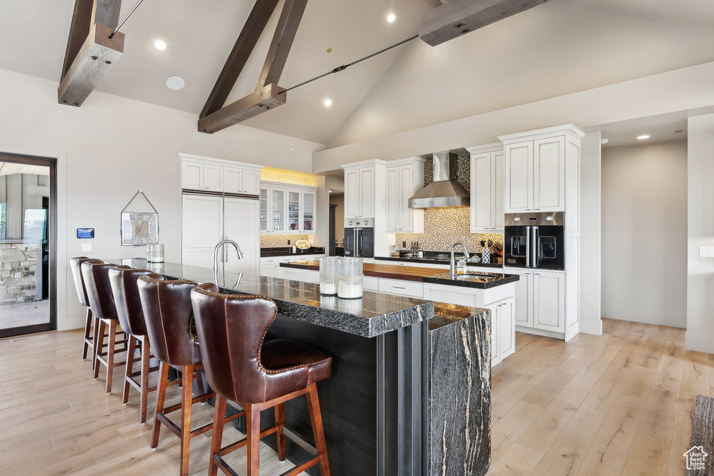 Kitchen with wall chimney exhaust hood, decorative backsplash, a large island, paneled refrigerator, and beam ceiling
