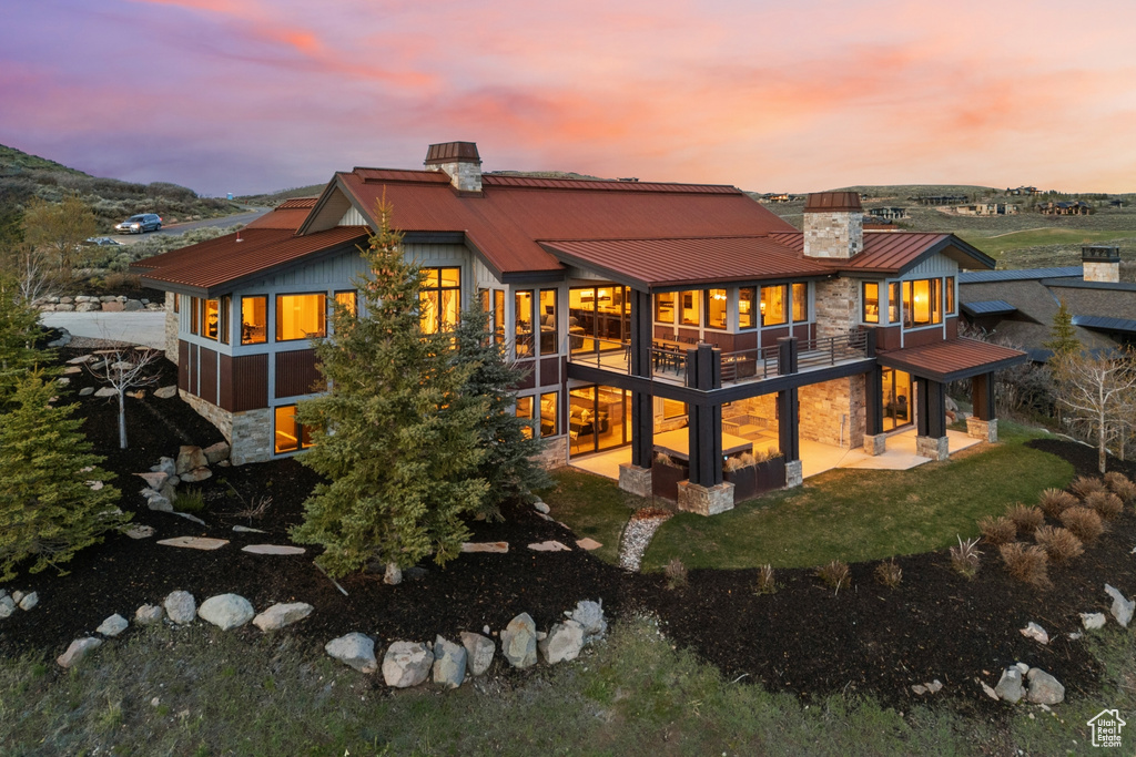 Back of house at dusk with stone siding, a chimney, metal roof, a patio area, and a standing seam roof