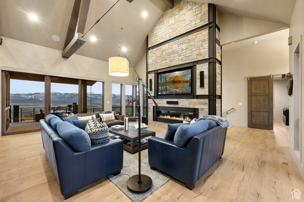 Living room featuring a stone fireplace, beamed ceiling, light wood-style flooring, and high vaulted ceiling