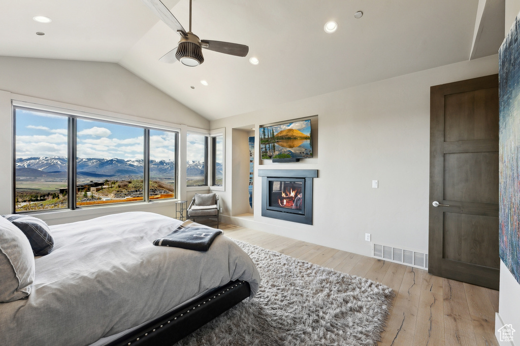 Bedroom featuring light wood-style flooring, recessed lighting, a glass covered fireplace, visible vents, and vaulted ceiling