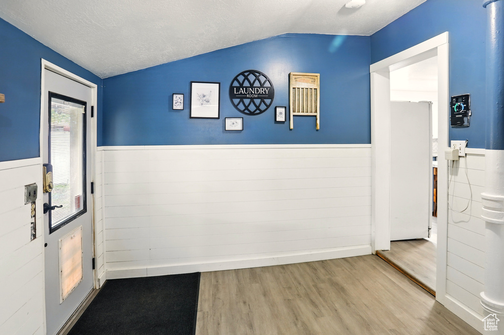 Doorway to outside with lofted ceiling, a wainscoted wall, wood finished floors, and a textured ceiling