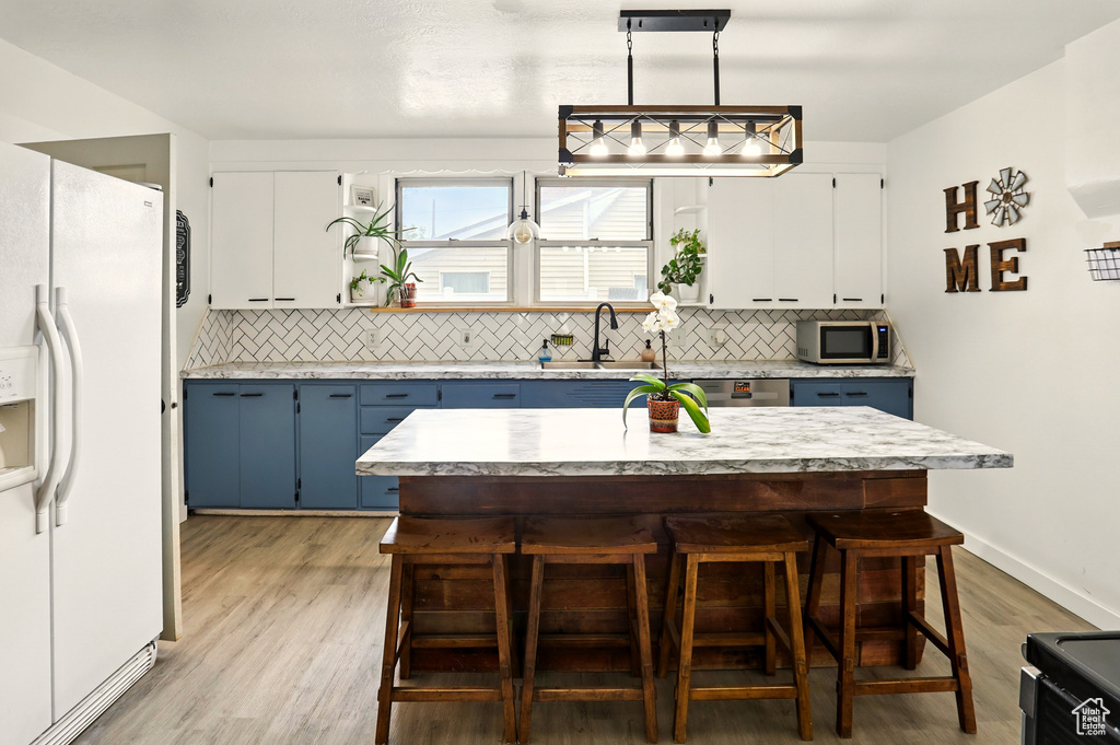 Kitchen with white fridge with ice dispenser, stainless steel microwave, blue cabinetry, a sink, and light countertops
