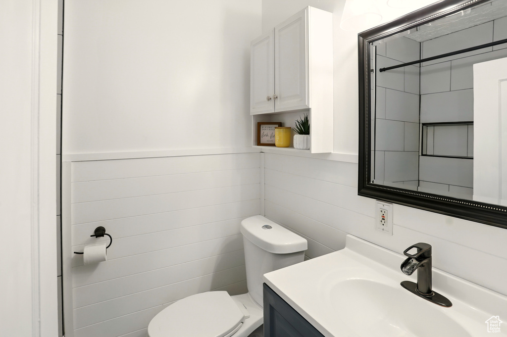 Bathroom with toilet, vanity, tile walls, and a wainscoted wall