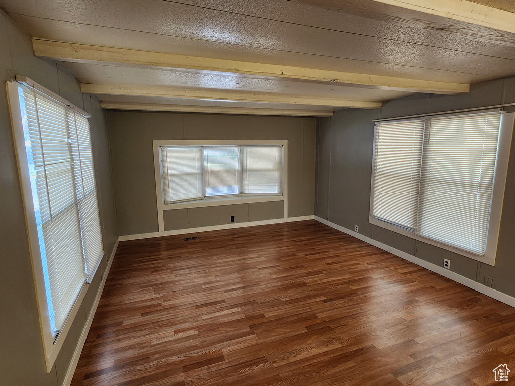 Spare room with beamed ceiling, wood finished floors, plenty of natural light, baseboards, and a textured ceiling