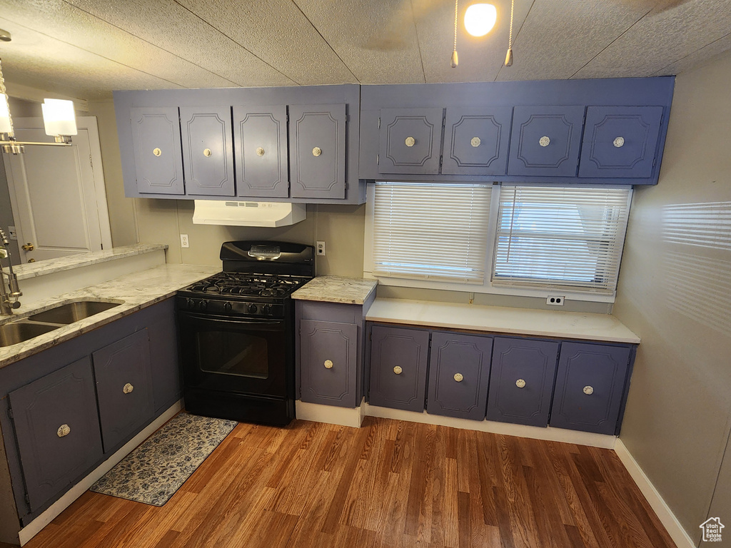 Kitchen featuring black gas stove, a sink, wood finished floors, under cabinet range hood, and gray cabinets