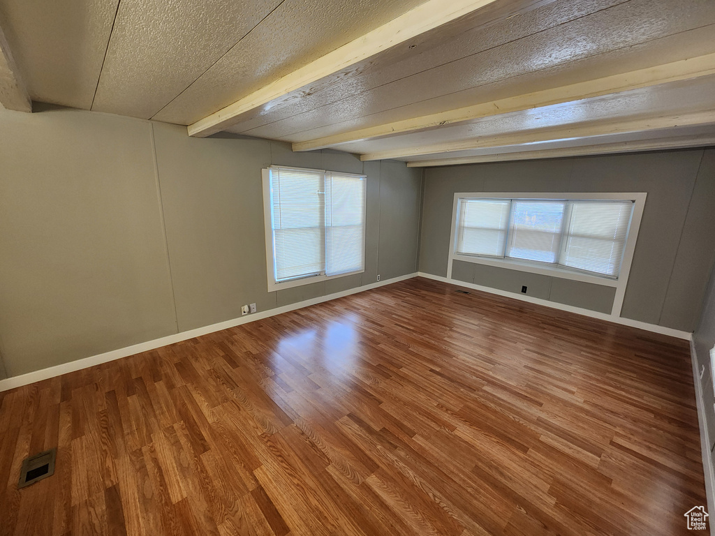 Spare room featuring a textured ceiling, beamed ceiling, wood finished floors, and baseboards