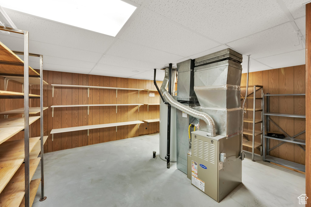 Unfinished below grade area with wooden walls, a paneled ceiling, and heating unit