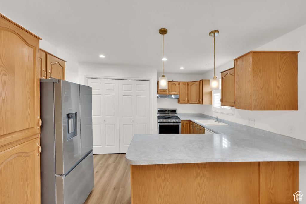 Kitchen featuring appliances with stainless steel finishes, a sink, a peninsula, light countertops, and recessed lighting