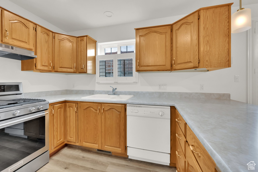Kitchen with stainless steel gas range oven, dishwasher, under cabinet range hood, a sink, and light wood finished floors