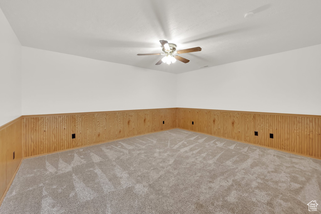 Carpeted spare room featuring a ceiling fan, a wainscoted wall, and wooden walls